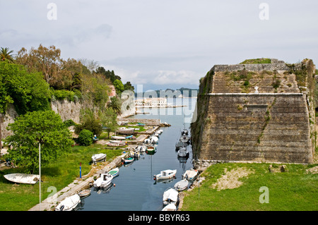 Pleasure boats moored in the defensive ditch alongside a formidable bastion of the Old Fortress, Corfu Town Stock Photo