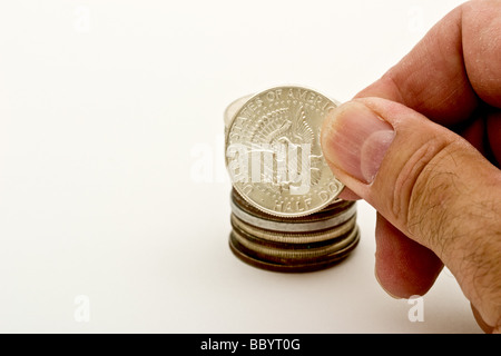 Fingers holding an American half dollar coin in front of a pile of coins Stock Photo