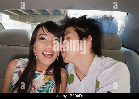 Chinese man kissing girlfriend in back of car Stock Photo