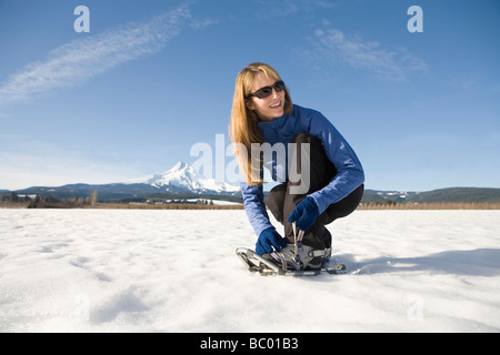 Young woman straps on snowshoes with Mt. Hood, Oregon in background. Stock Photo