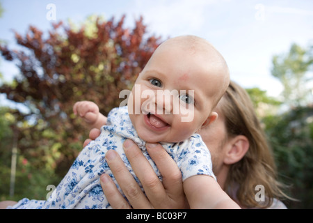 three month old baby girl being swung up by parent, smiling at camera Stock Photo