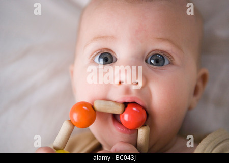 three month old baby girl grasping and mouthing a teething ring made of wooden beads, chewing on toy Stock Photo