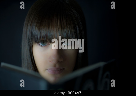 Young teenage girl aged fourteen looking seriously at the camera over a book Stock Photo