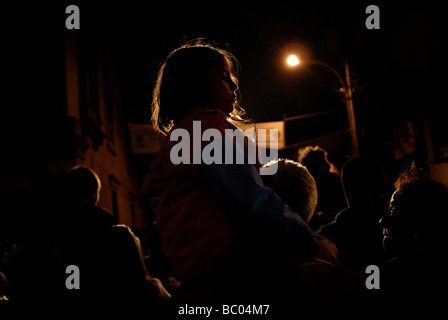 A young Catholic girl sits atop her parent's shoulders during a night religious procession to celebrate holy week in Merida, Ven Stock Photo