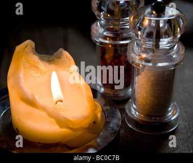 Candle Burning in Subdued Light by Salt and Pepper Mills Stock Photo