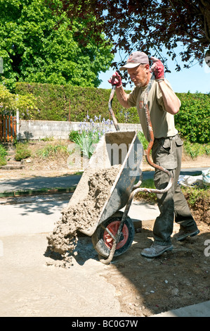 Building worker pouring concrete from wheelbarrow for vehicle hard standing. Stock Photo