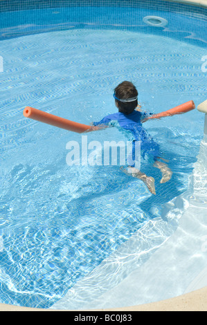 Boy aged 6 swims with the aid of a woggle or noodle in a pool in Majorca, Spain Stock Photo