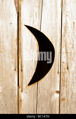 Half moon carved into door of old fashioned wooden outhouse Stock Photo