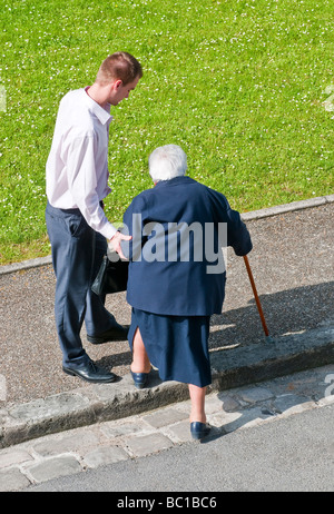 Young man helping elderly woman onto pavement - France. Stock Photo