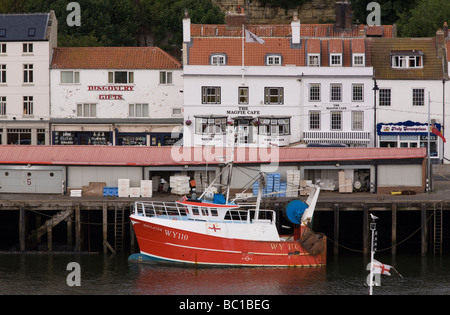 A fishing trawler moored in front of the fish quay and the Magpie Cafe, famous fish and chip restaurant - Whitby Stock Photo