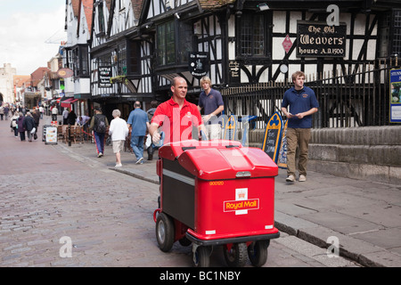 A Postman pushing a Royal Mail post trolley delivering mail in a city street. Canterbury Kent England UK Britain Stock Photo
