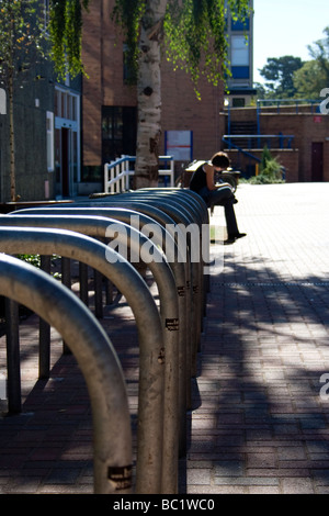 A student reading a book outside in the sunshine at the Gipsy Lane campus of Oxford Brookes university, Oxford. Empty bike racks Stock Photo