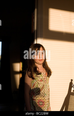 Nine year old girl stands in doorway in early evening light Stock Photo