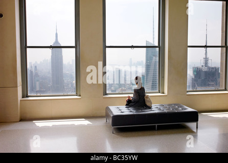 A woman sitting at the top of the Rockefeller Centre in New York looking at the Empire State Building Stock Photo
