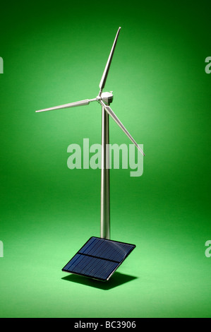 A small metal wind turbine on a green background with a small solar panel Stock Photo