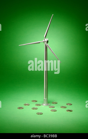 A small metal wind turbine on a green background with currency coins Stock Photo