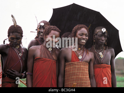 Six smiling Maasai warriors Moran shelter under umbrella in rain shower Masai Mara National Reserve Kenya East Africa Stock Photo