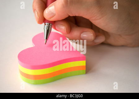 Hand holding pen writing on heart shaped colorful sticky notes Stock Photo