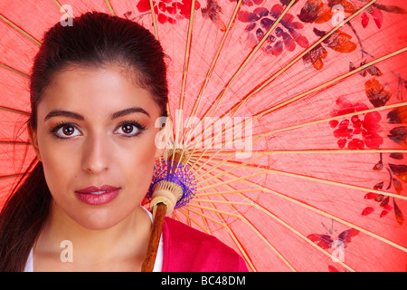 Beauty shot of a young brunette woman with brown eyes holding a red chinese umbrella Stock Photo