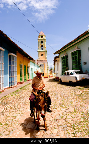 Old man riding donkey on cobblestone scene with old car in street scene with old church of the old colonial city Stock Photo