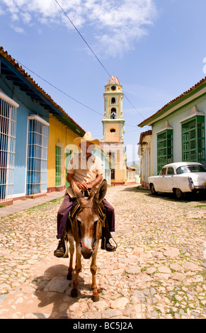 Old man riding donkey on cobblestone scene with old car in street scene with old church of the old colonial city Stock Photo