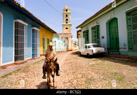 Old man riding donkey on cobblestone scene with old car in street scene with old church of the old colonial city Stock Photo