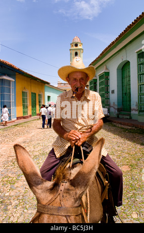 Old man riding donkey on cobblestone scene with old car in street scene with old church of the old colonial city Stock Photo