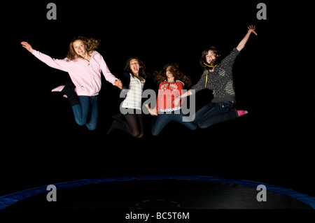 4 young early teens girl friends jumping on a trampoline at night on a birthday 'sleepover'.