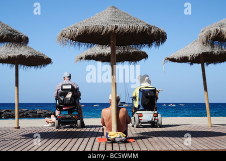 Couple on mobility scooters looking out to sea from Los Cristianos beach on Tenerife in The Canary Islands Stock Photo