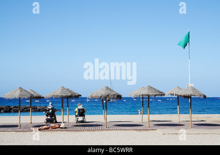 Couple on mobility scooters looking out to sea from Los Cristianos beach on Tenerife in The Canary Islands Stock Photo