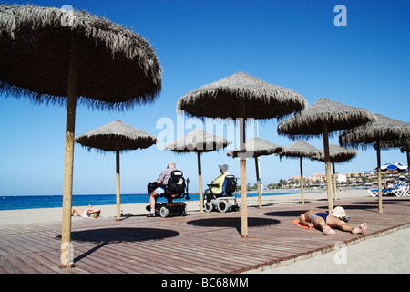 Couple on mobility scooters looking out to sea from Los Cristianos beach on Tenerife in The Canary Islands Stock Photo