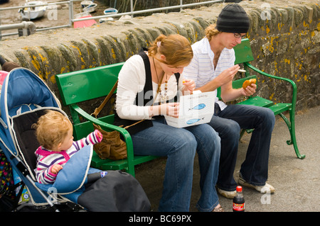 Husband and Wife Enjoying Fish and Chips On a Bench with Their Child In a Pushchair Stock Photo