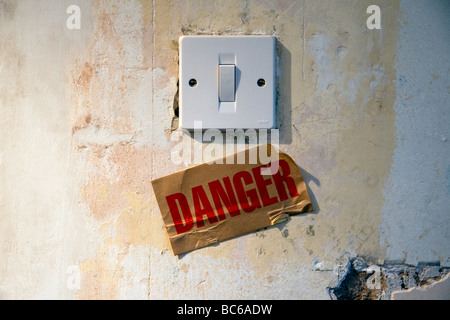 A lightswitch on a dilapidated wall with a sign underneath reading "Danger". Stock Photo
