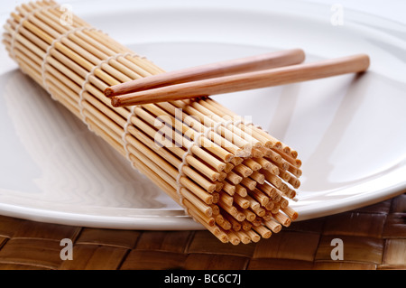 a horizontal macro of a pair of chopsticks and a sushi rolling mat on a white plate Stock Photo