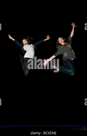 2 young early teens girl friends jumping on a trampoline while laughing at night on a birthday 'sleepover'.