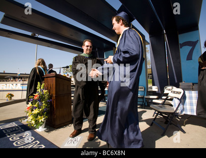 Wearing cap and gown carrying his new diploma a graduating high school senior reaches out to shake hands with a faculty member Stock Photo