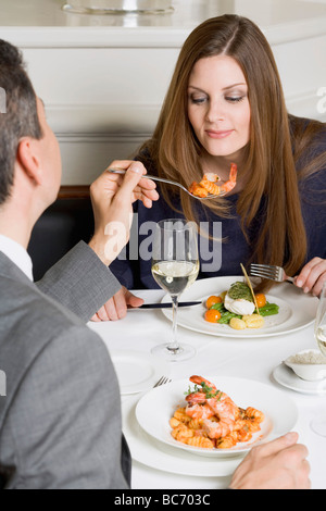 Man offering woman prawn on fork in restaurant - Stock Photo