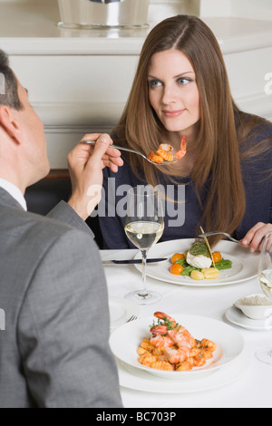 Man offering woman prawn on fork in restaurant - Stock Photo