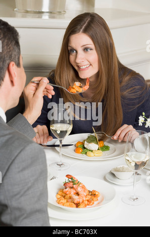 Man offering woman prawn on fork in restaurant - Stock Photo