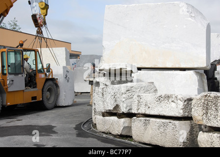 mobile crane moving giant blocks of pure white Carrara marble in the holding yard of Cave Michelangelo Stock Photo
