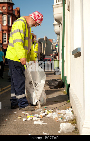 Refuse collectors picking up litter left on the street when seagulls have ripped open bin bags left on the pavement UK Stock Photo