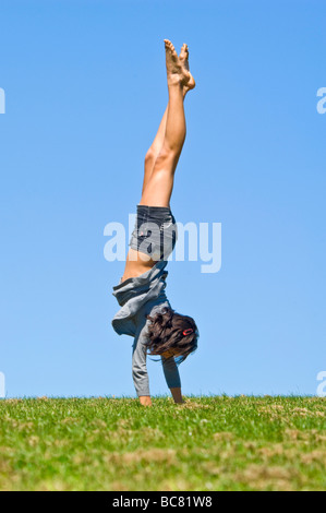 Vertical portrait of an attractive young teenage girl doing a handstand on the grass on a bright sunny day Stock Photo