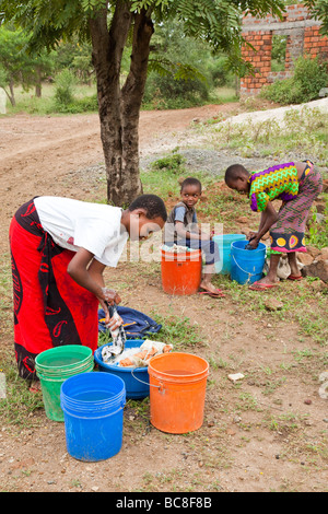 African girls washing laundry by hand in brightly coloured buckets ...