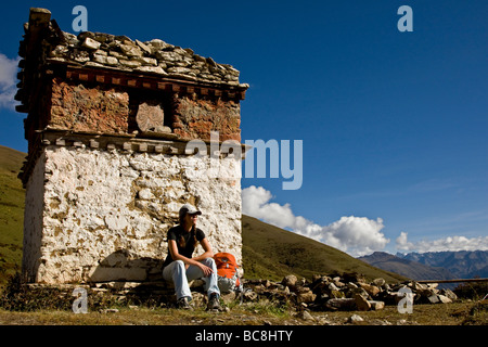 A woman sitting next to a prayer temple in Bhutan. This is situated along a trail at around 14,000ft. Stock Photo