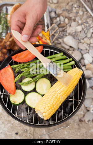 Hand brushing corn cob on barbecue with oil - Stock Photo