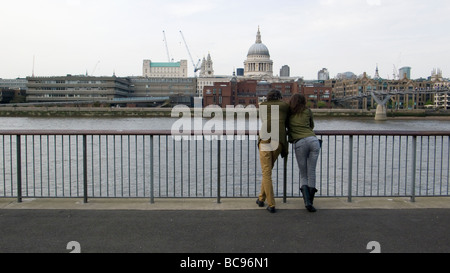 Couple leaning on a railing over a river with the city skyline behind Stock Photo