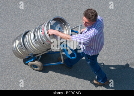 Beer delivery driver with metal kegs on 2-wheeled truck - France. Stock Photo