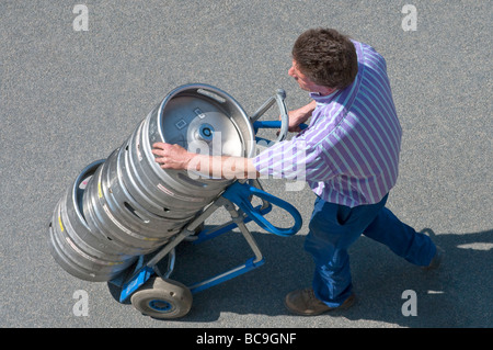 Beer delivery driver with metal kegs on 2-wheeled truck - France. Stock Photo