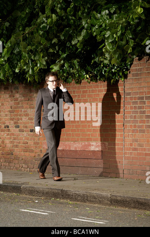 A suited young professional man walks along a urban street while talking on a mobile phone in Marylebone, London, England. Stock Photo