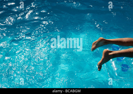Mans feet on a lilo in a blue swimming pool Stock Photo